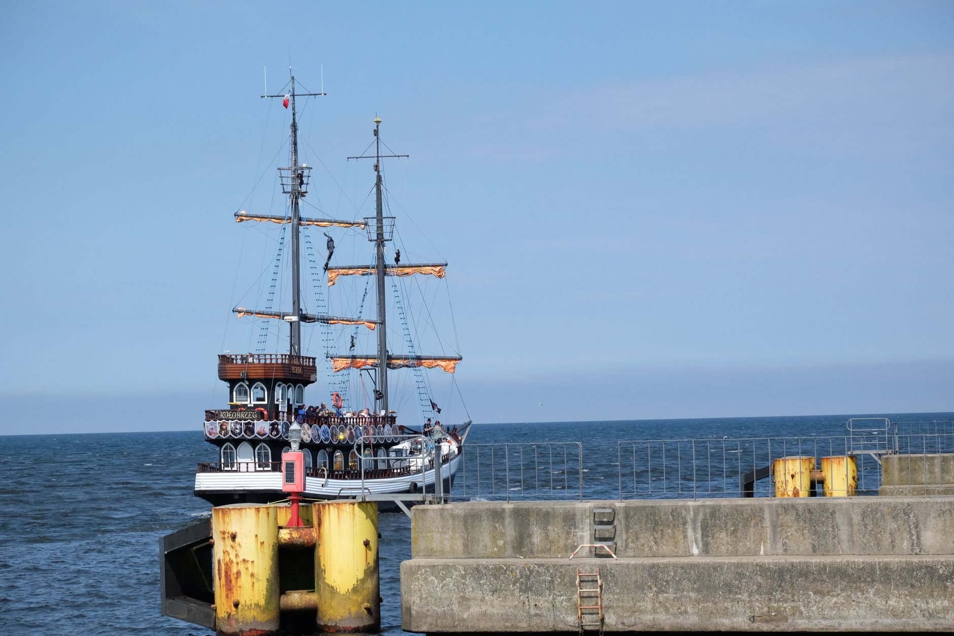 A classic pirate ship docked at a concrete harbor under a clear blue sky.