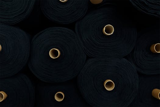 Circular rolls of black fabric stacked closely, showcasing textiles in an industrial setting.