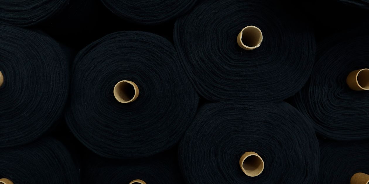 Cuộn vải polyester đen xếp chồng trong nhà máy dệt — độ tin cậy nhà cung cấp vải