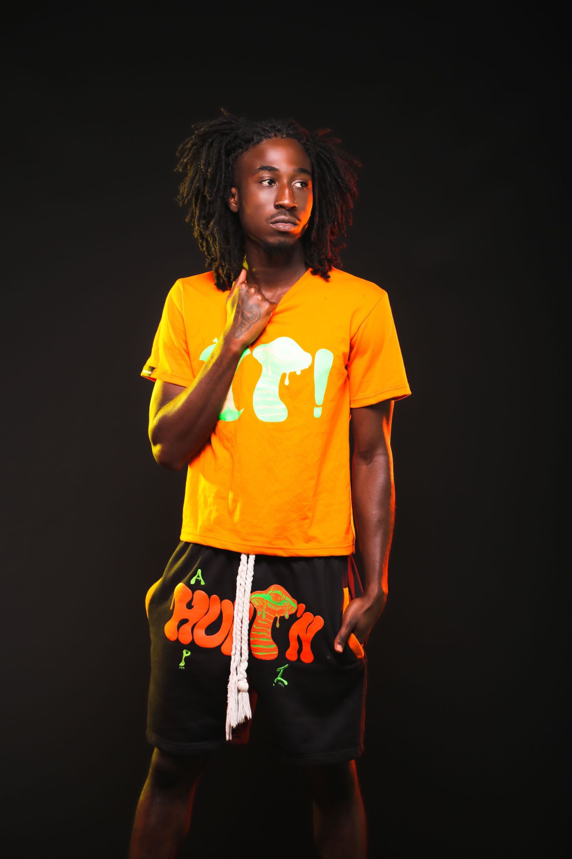 Young man posing in vibrant orange fashion against dark background.