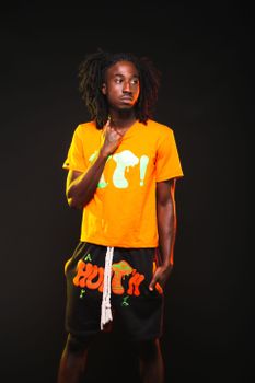Young man posing in vibrant orange fashion against dark background.