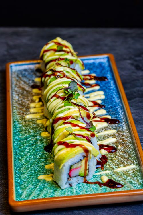 Free Vegetarian sushi roll with avocado and sauce drizzles on a vibrant ceramic plate. Stock Photo