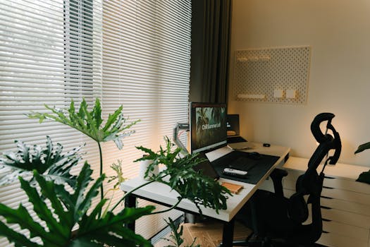 A stylish home office with a desk, chair, and lush green plants near a window with blinds.