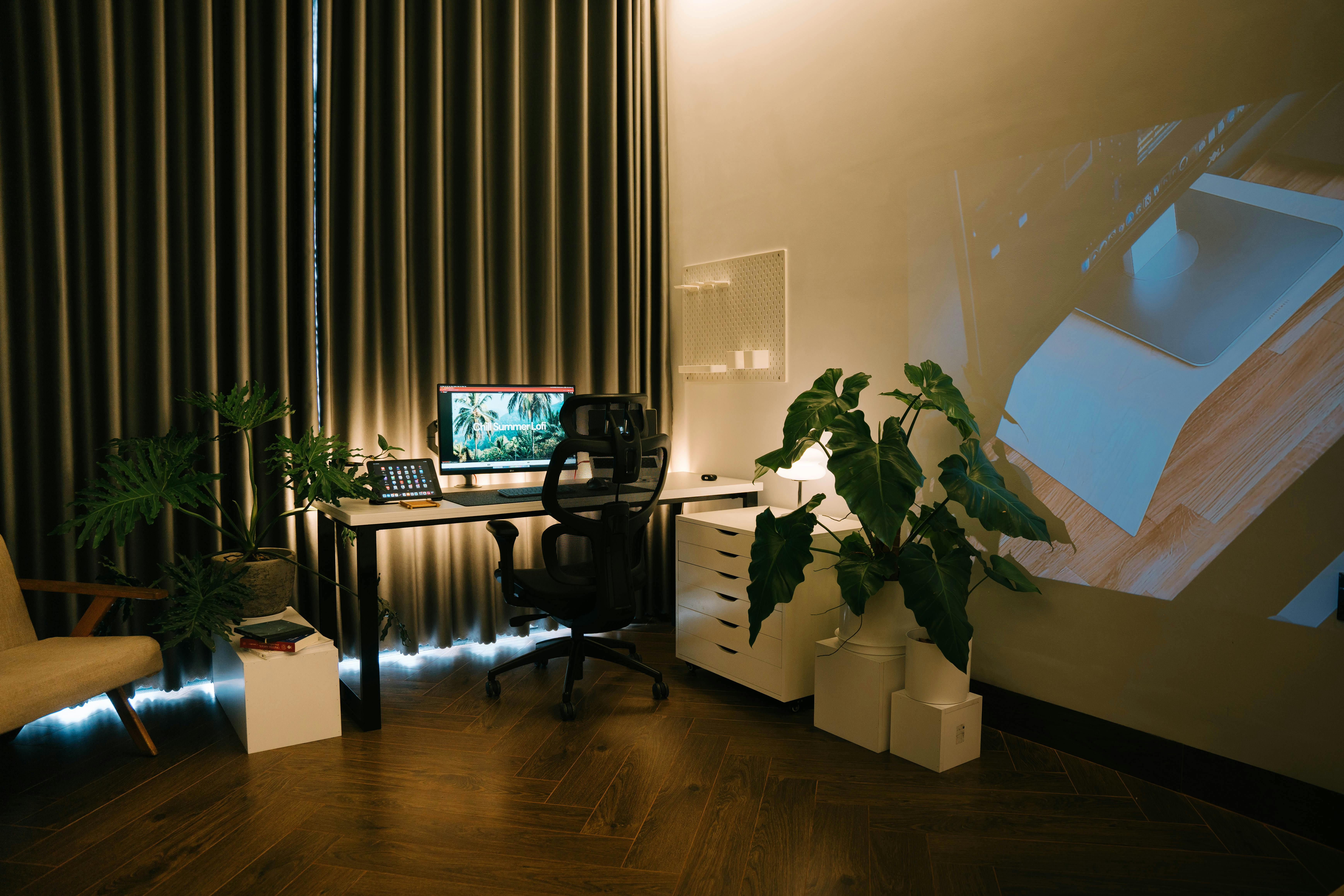 Cozy home office setup with computer, plants, and warm lighting, perfect for productivity.