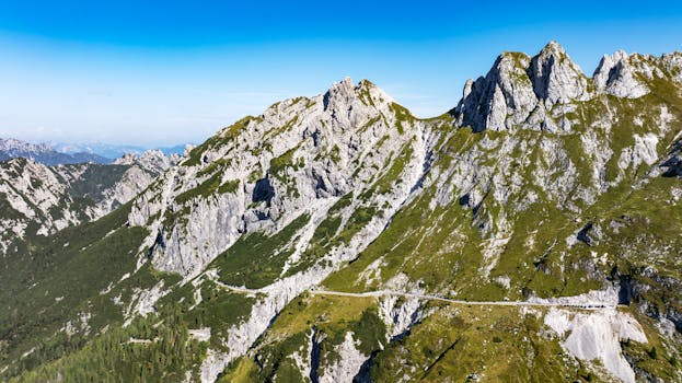 A stunning aerial view of rocky mountains and winding roads in Slovenia under clear blue skies.