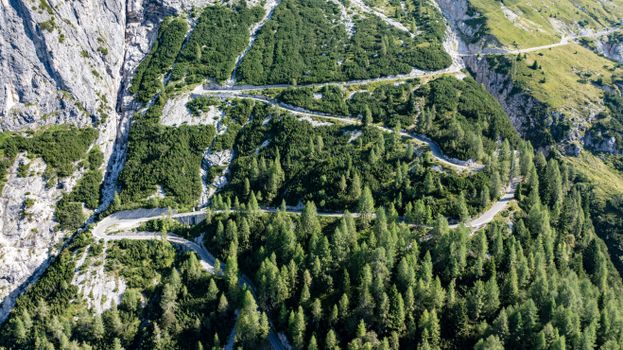 Aerial view of a winding mountain road amidst lush green forest and rugged cliffs.
