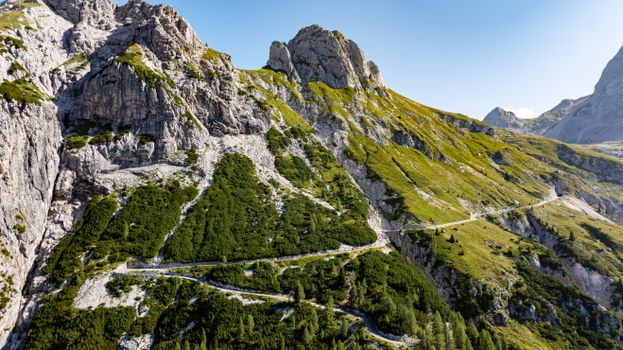 A breathtaking aerial view of a winding path through lush green mountains under a clear blue sky in Slovenia.