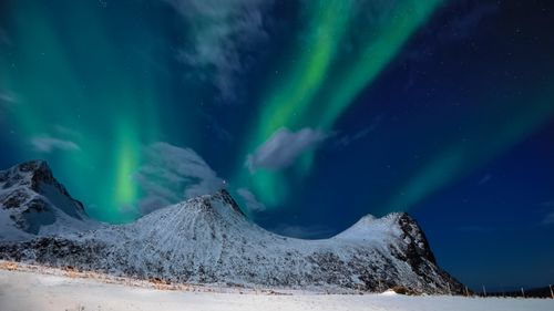 Free Captivating aurora borealis illuminating snowy peaks in Myrland, Norway. Stock Photo
