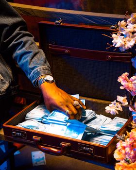 Person reaches into a suitcase overflowing with cash. Vibrant and dramatic lighting.