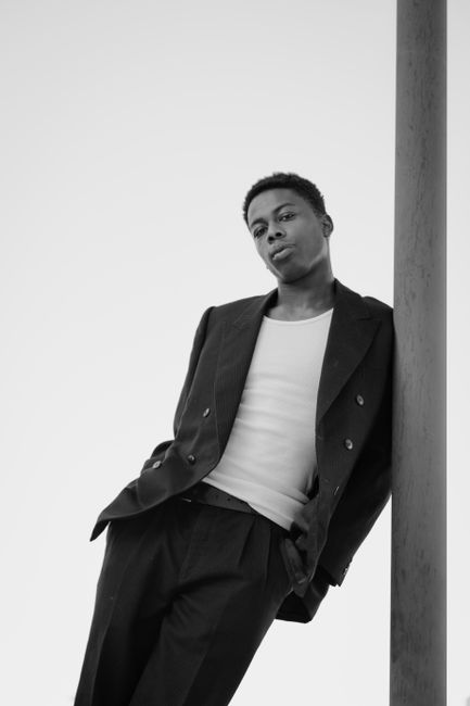 Monochrome portrait of a man leaning against a pole in urban fashion.