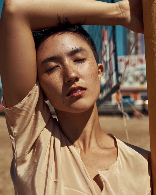 Close-up Photo of Woman with Freckles Posing with Her Eyes Closed Placing Her Right Arm on Head