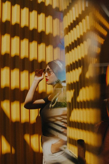 A stylish woman poses outdoors with sunlit geometric shadows and bold fashion.