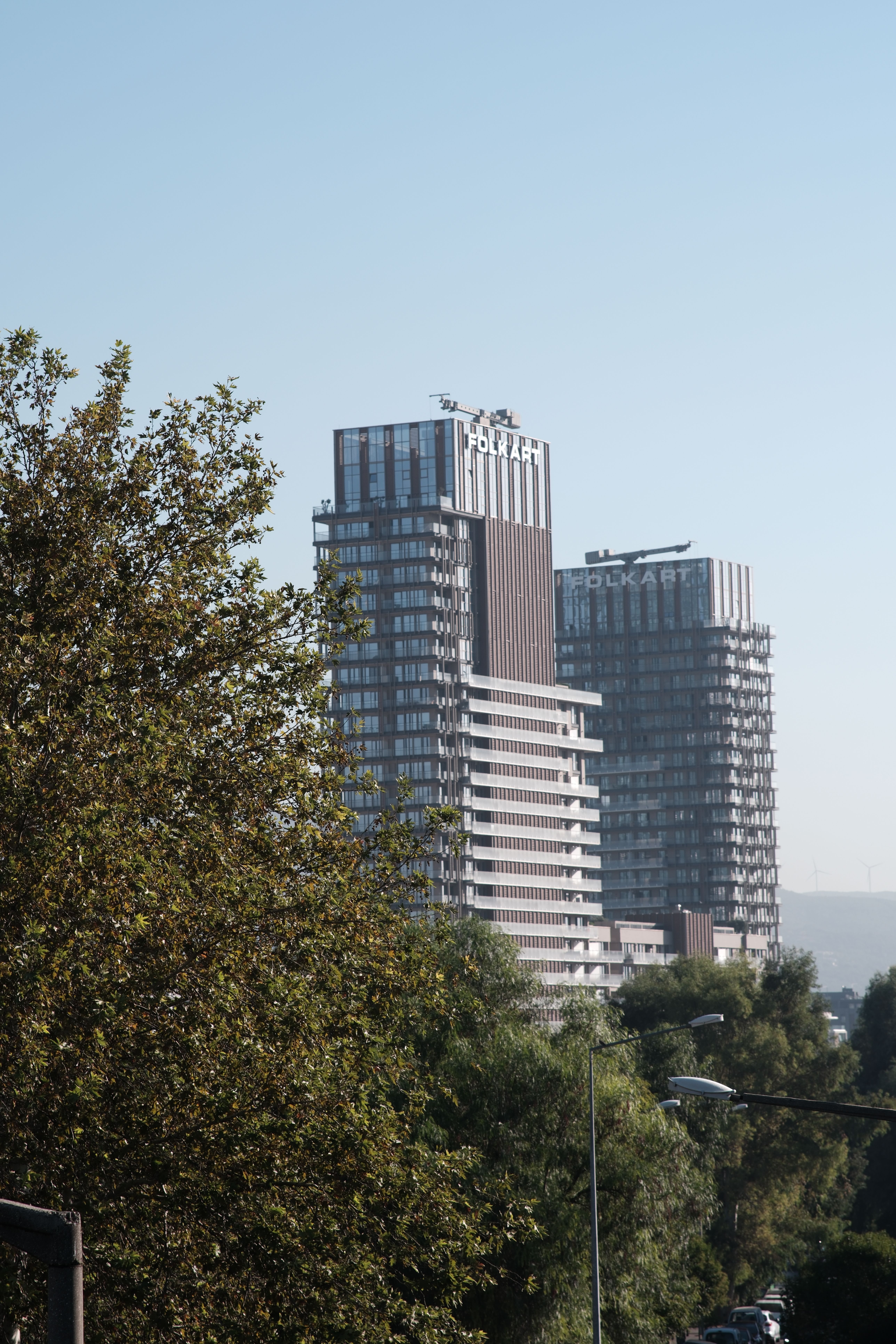 Skyscrapers rise above lush greenery in Bornova, İzmir, on a sunny day.