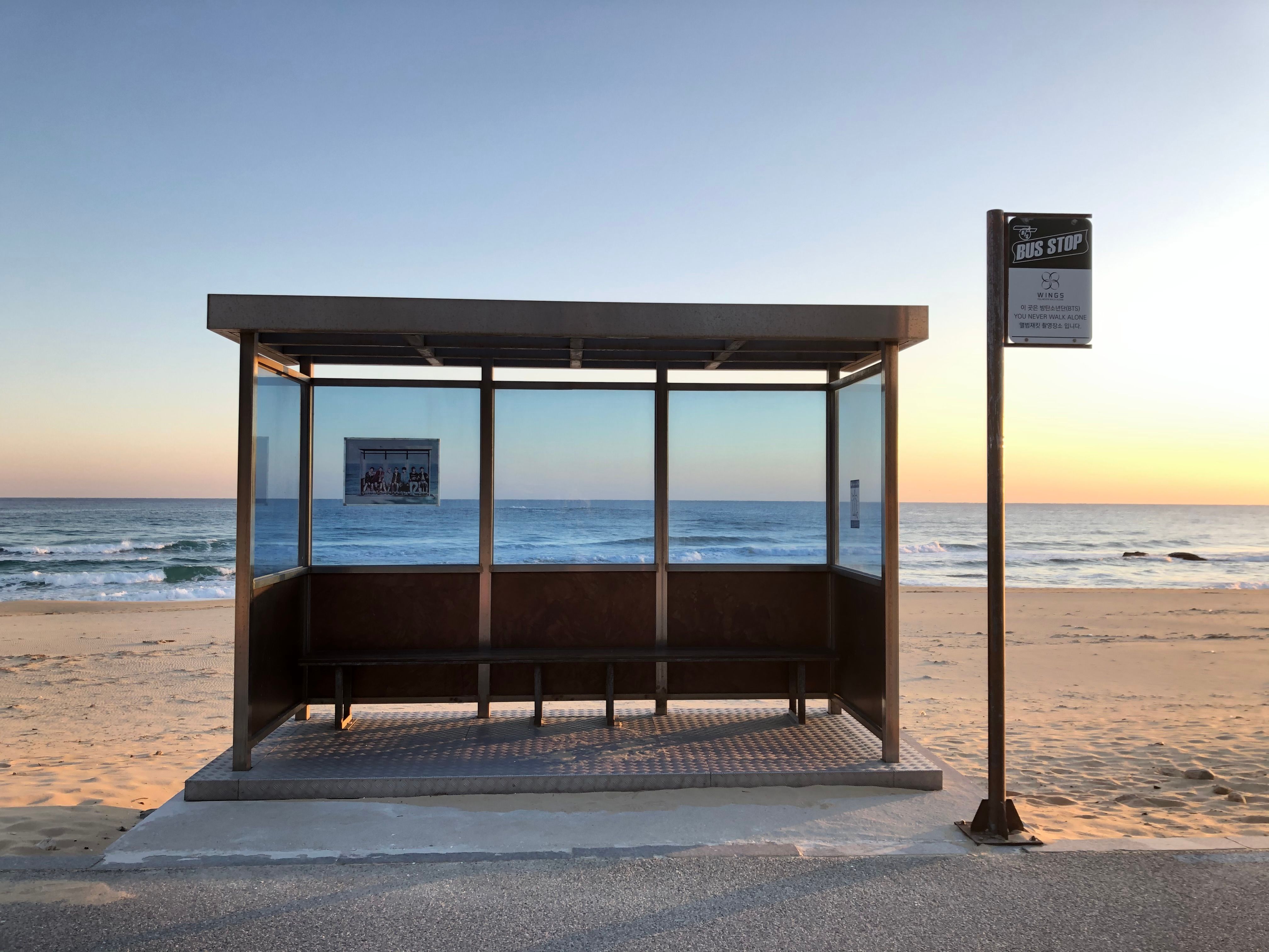 Bus stop on a sandy beach with ocean view at sunrise, creating a peaceful scene.