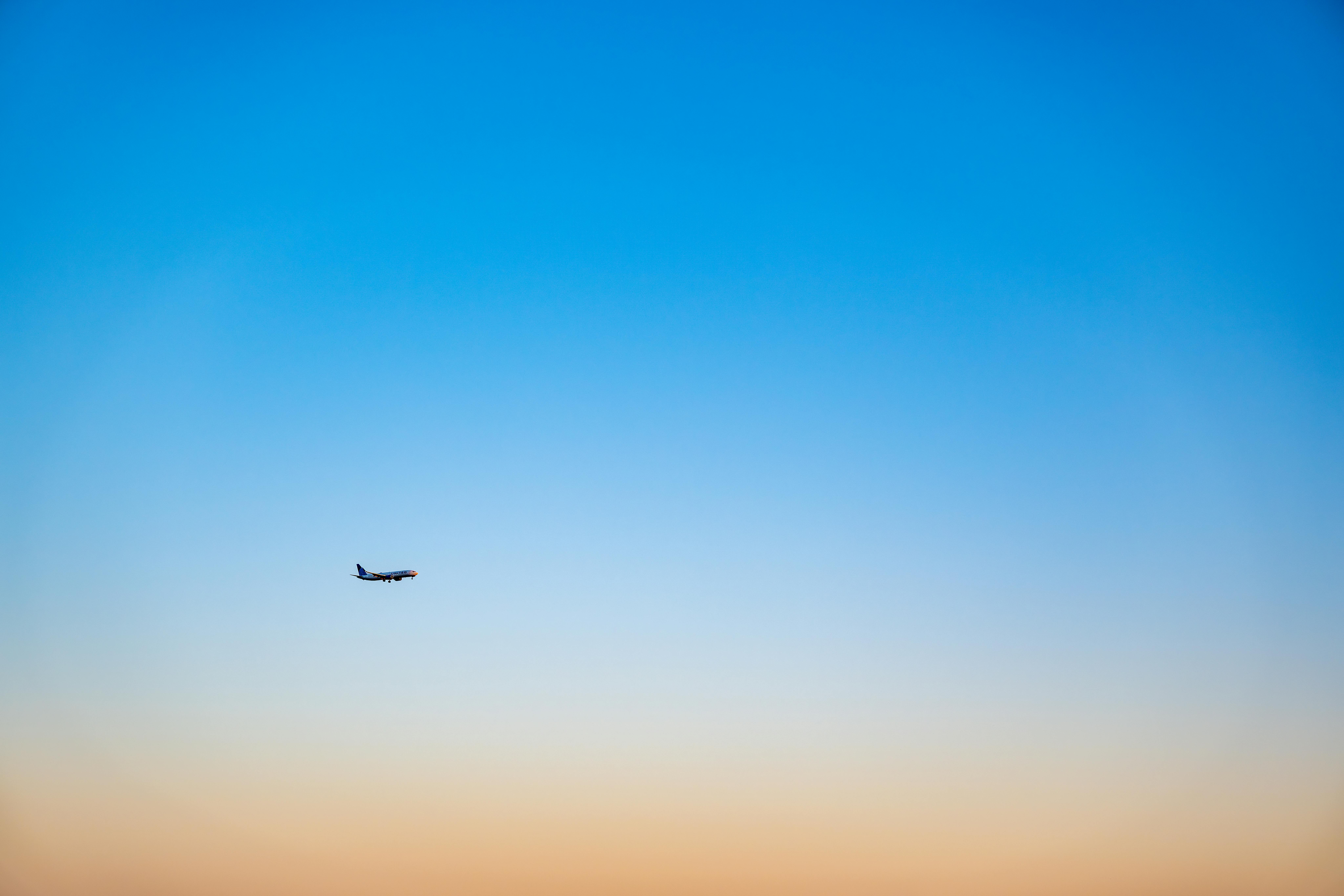 A lone airplane flying in a gradient blue and orange sky during sunset, creating a serene travel backdrop.
