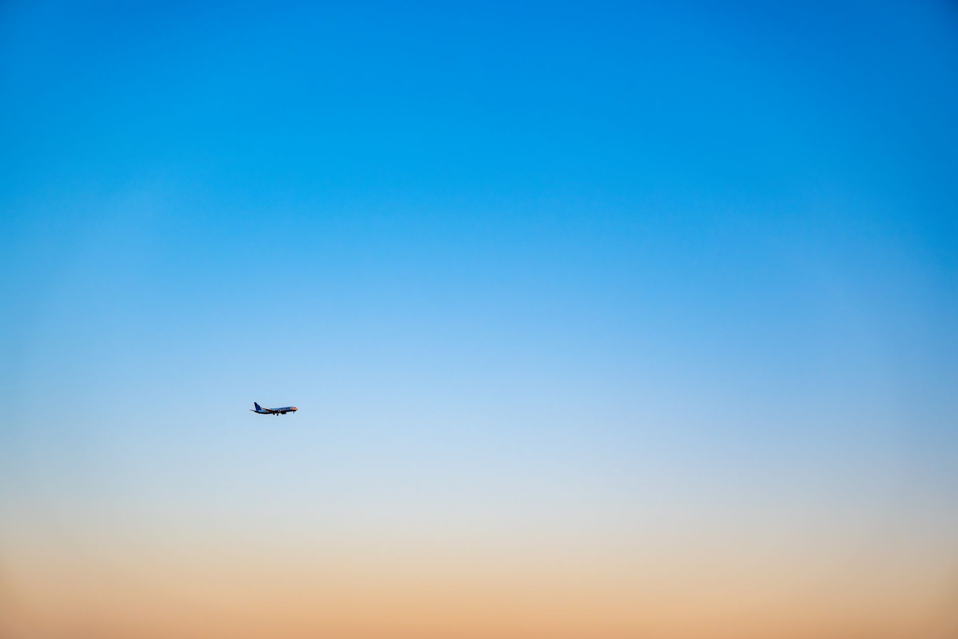 A lone airplane flying in a gradient blue and orange sky during sunset, creating a serene travel backdrop.
