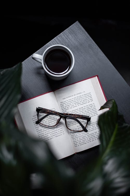 Free Eyeglasses On Opened Book Beside Cup Of Coffee On Table Stock Photo