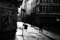 一张黑白照片以戏剧性的手法，捕捉了黄昏时分空荡荡的城市街道，街道上投下深深的阴影，映衬着城市建筑