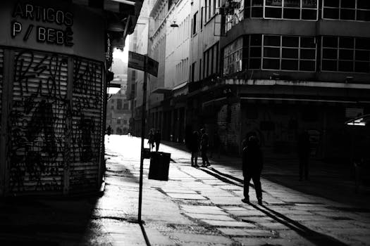 一张黑白照片以戏剧性的手法，捕捉了黄昏时分空荡荡的城市街道，街道上投下深深的阴影，映衬着城市建筑