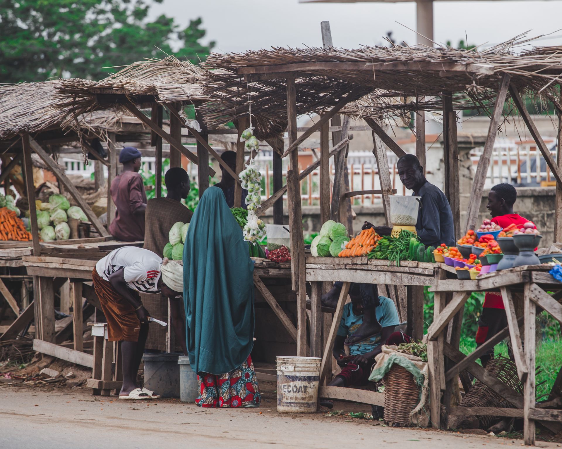 A bustling local market scene featuring fresh fruits and vegetables with diverse people interacting under rustic stalls.