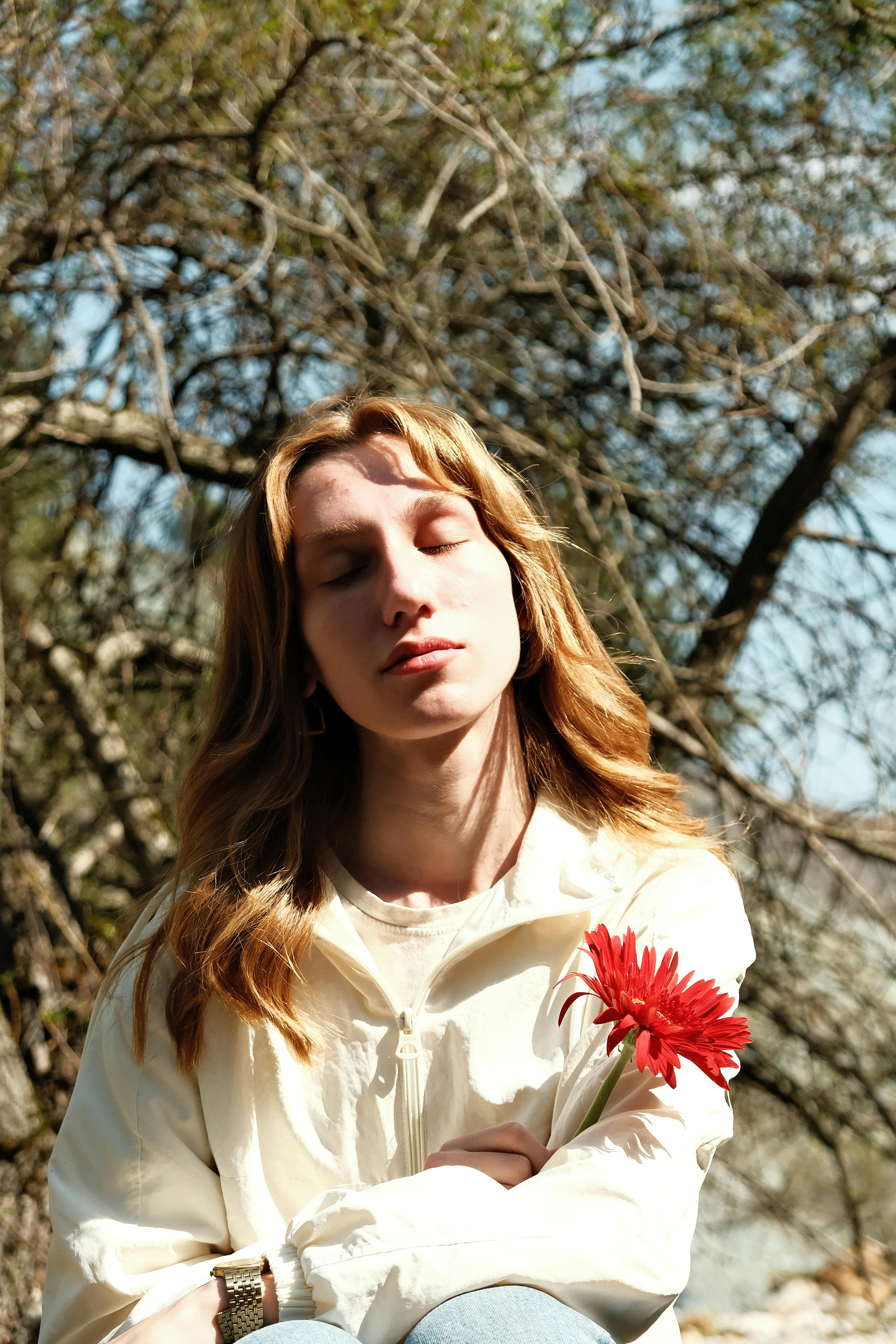 Young woman enjoying sunshine outdoors holding a red flower.