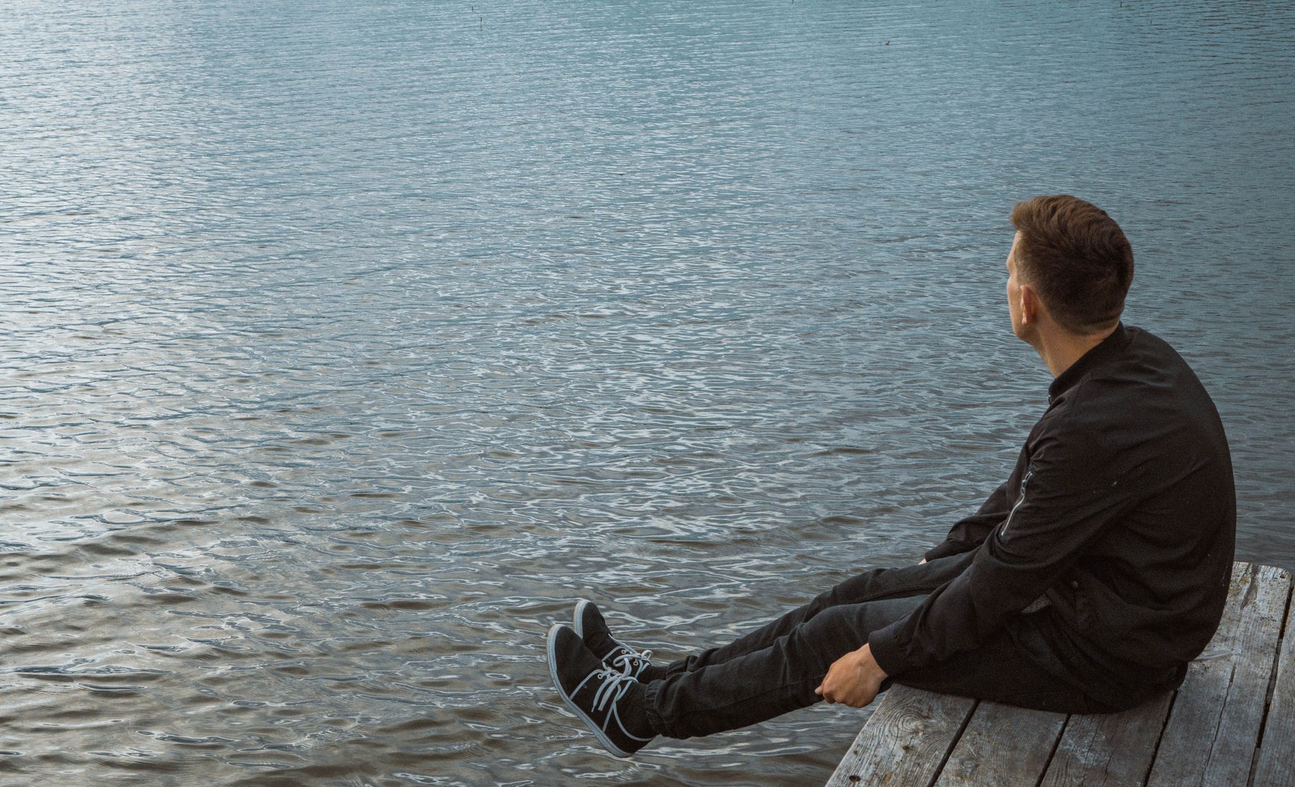 A man sits on a wooden dock, relaxing and enjoying the serenity of the tranquil water