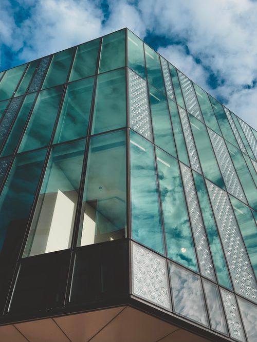 Free A contemporary glass building reflecting clouds under a blue sky. Stock Photo