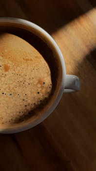 Artistic close-up of a coffee cup with rich foam and texture, sunlight casting a warm glow.
