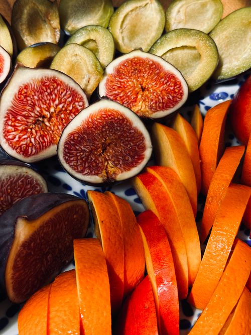 Free Colorful display of figs, oranges, and mango slices on a decorative plate. Stock Photo