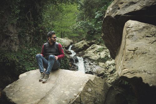 Free A young man sits on a rock near a waterfall in Beni M Tir, Tunisia, enjoying nature. Stock Photo