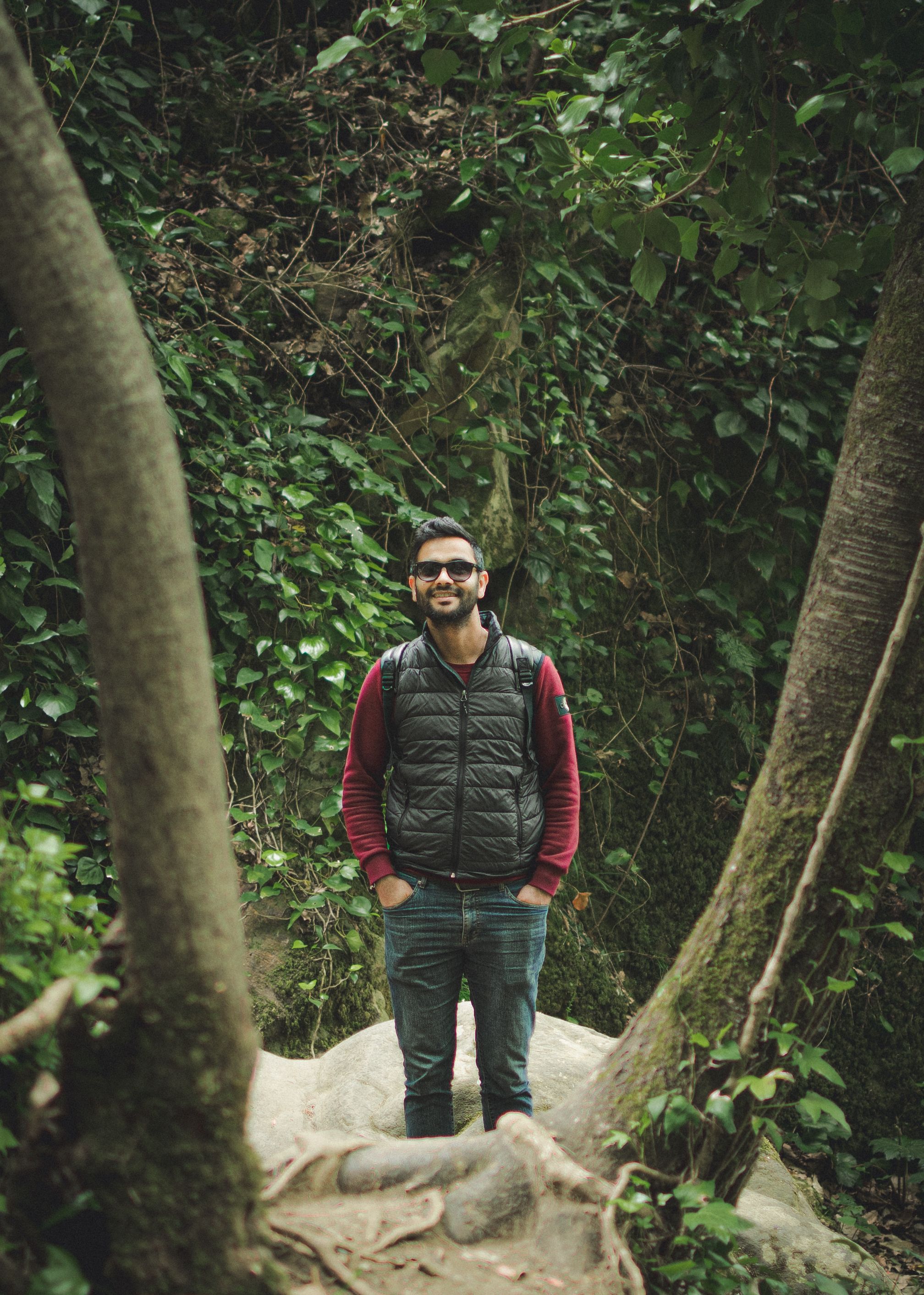 Portrait of a young man with sunglasses standing in a vibrant forest in Jendouba, Tunisia, showcasing nature's beauty.