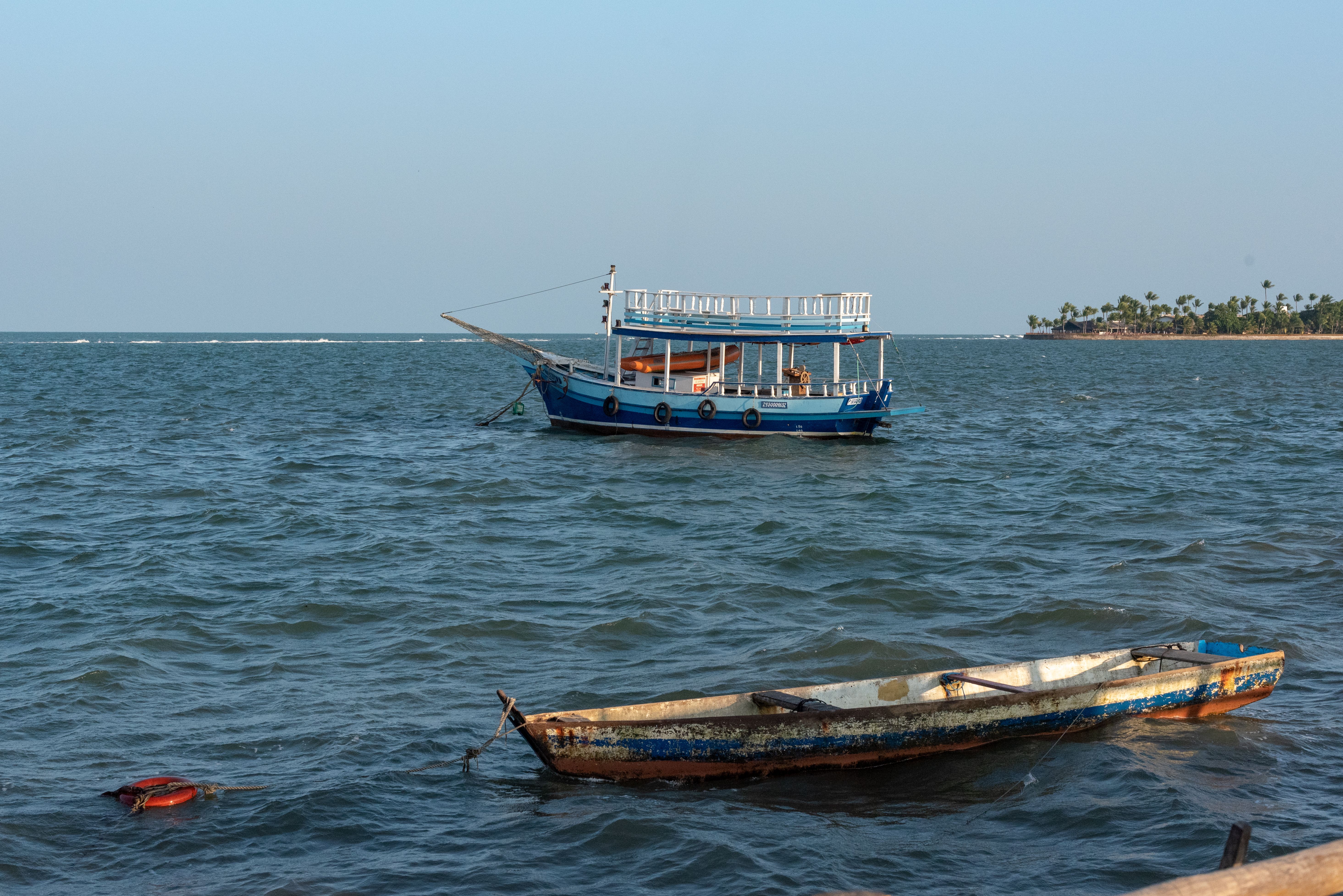 A traditional boat floats on the ocean near Porto Seguro, Brazil, under the clear blue sky.