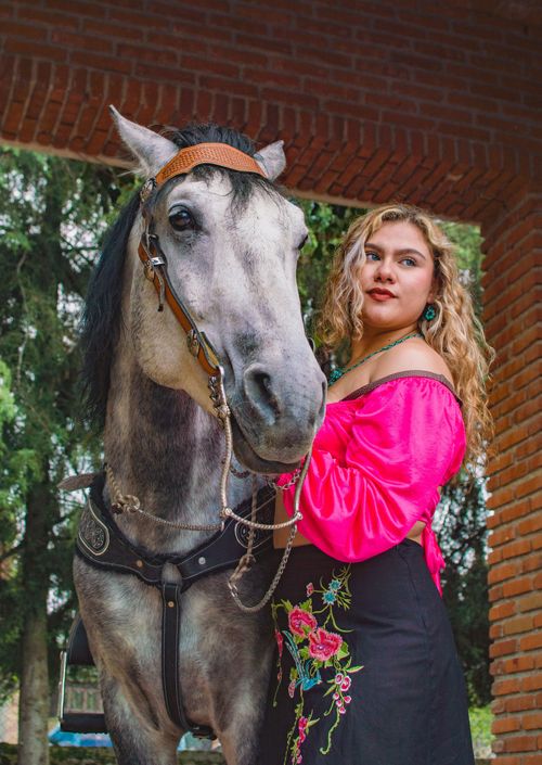 Free A woman in traditional Mexican attire poses beside a horse under a brick archway in San Bartolomé Xicomulco. Stock Photo
