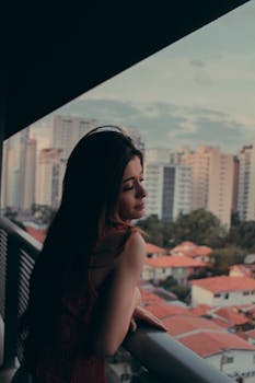A serene woman enjoys a moment on a balcony with cityscape views at dusk.
