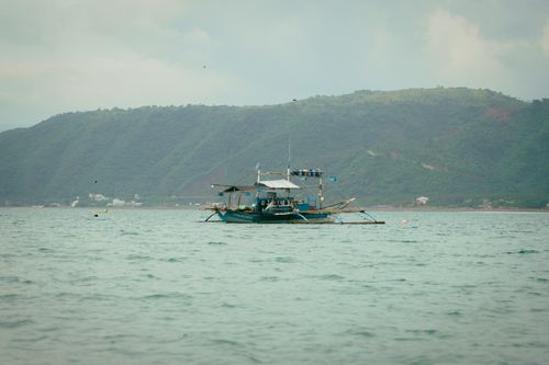 Free A traditional fishing boat floating on a calm sea against a mountainous backdrop Stock Photo