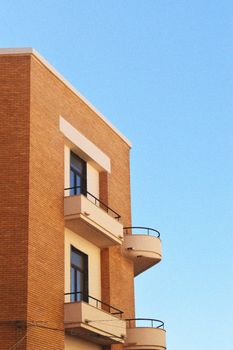 Minimalist architecture featuring a brick building with balconies against a clear blue sky.