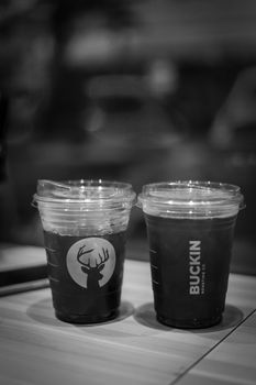 Black and white image of two iced coffee cups on a table with a blurred background.