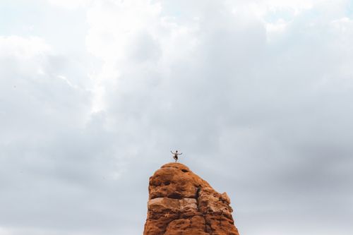 Free A lone individual practices yoga on a towering rock formation under a cloudy sky. Stock Photo