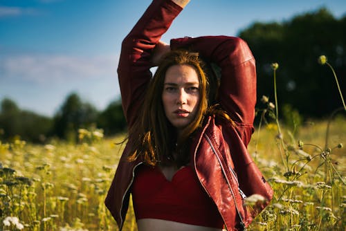 Free Photo of Woman in Red Leather Jacket and Red Crop Top Standing in Flower Field Raising Her Hands Stock Photo