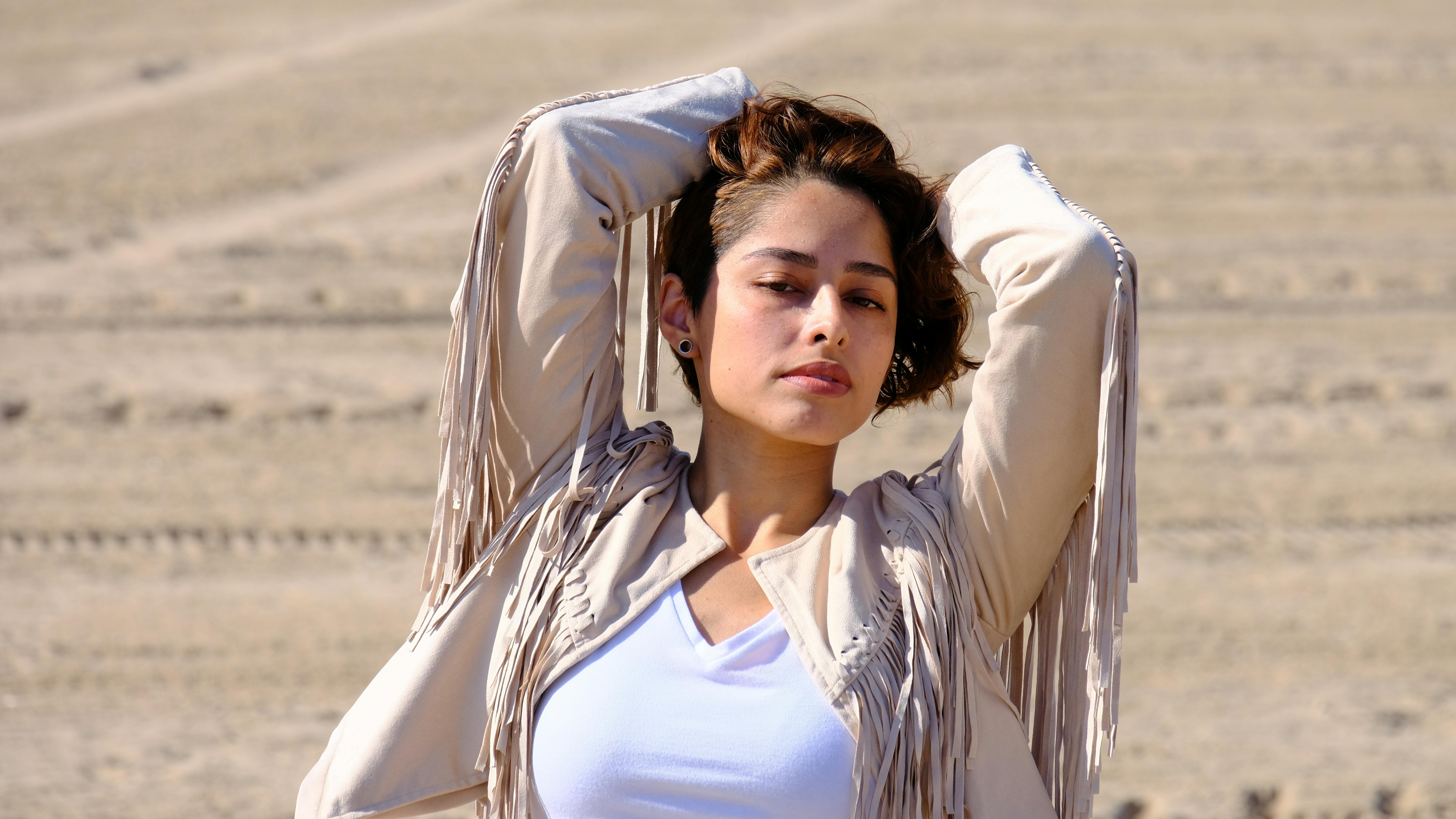 Stylish woman striking a pose in a fringe jacket on a sunny day outdoors.