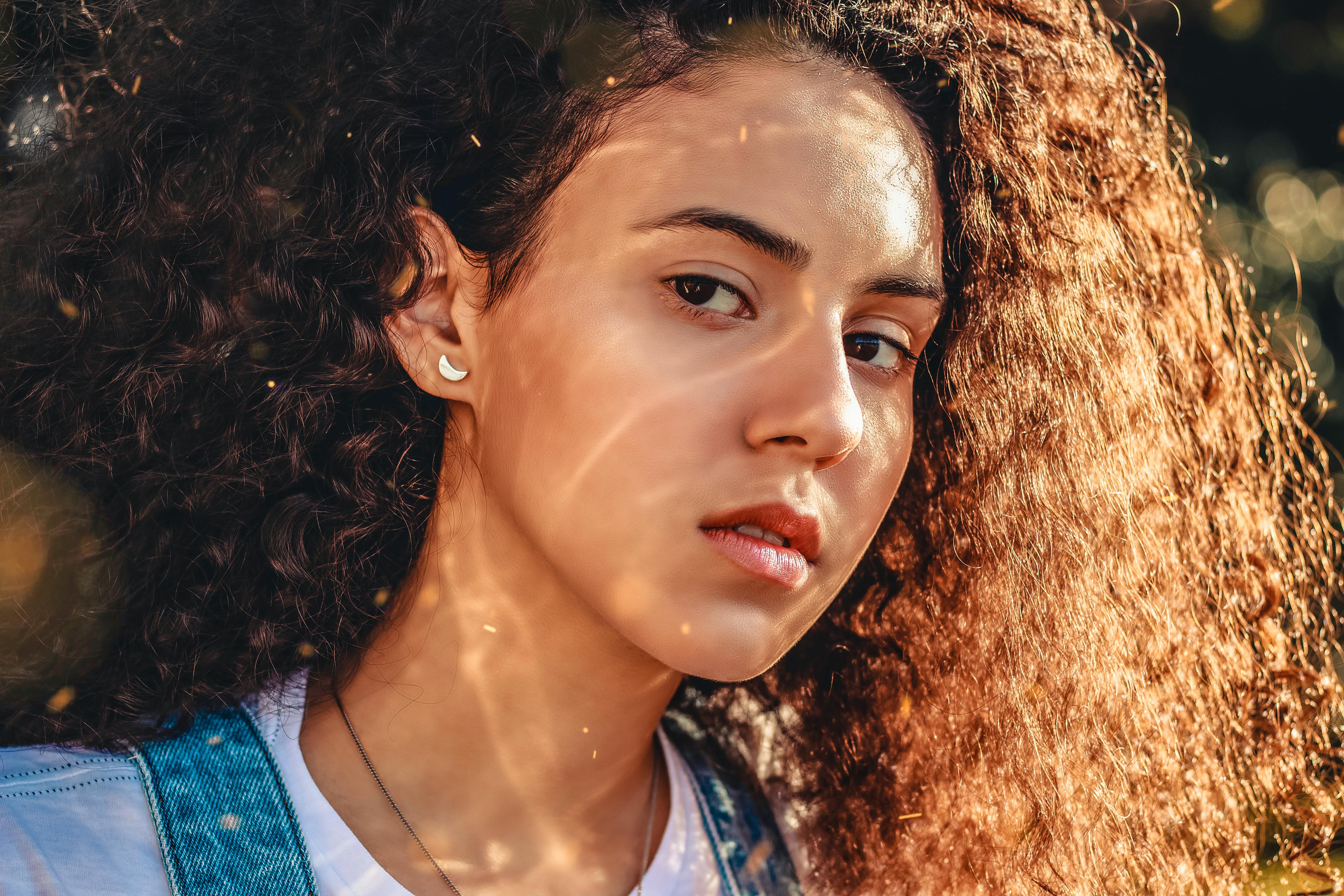 一位年轻卷发女子的特写肖像，在户外自然光线下，传达出充满活力与年轻的精髓