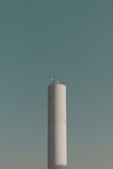 A tall white telecommunications tower stands against a clear blue sky, capturing a minimalist design.