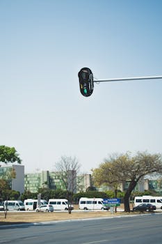 城市交通信号灯旁，晴天的城市环境中停有多辆白色小巴