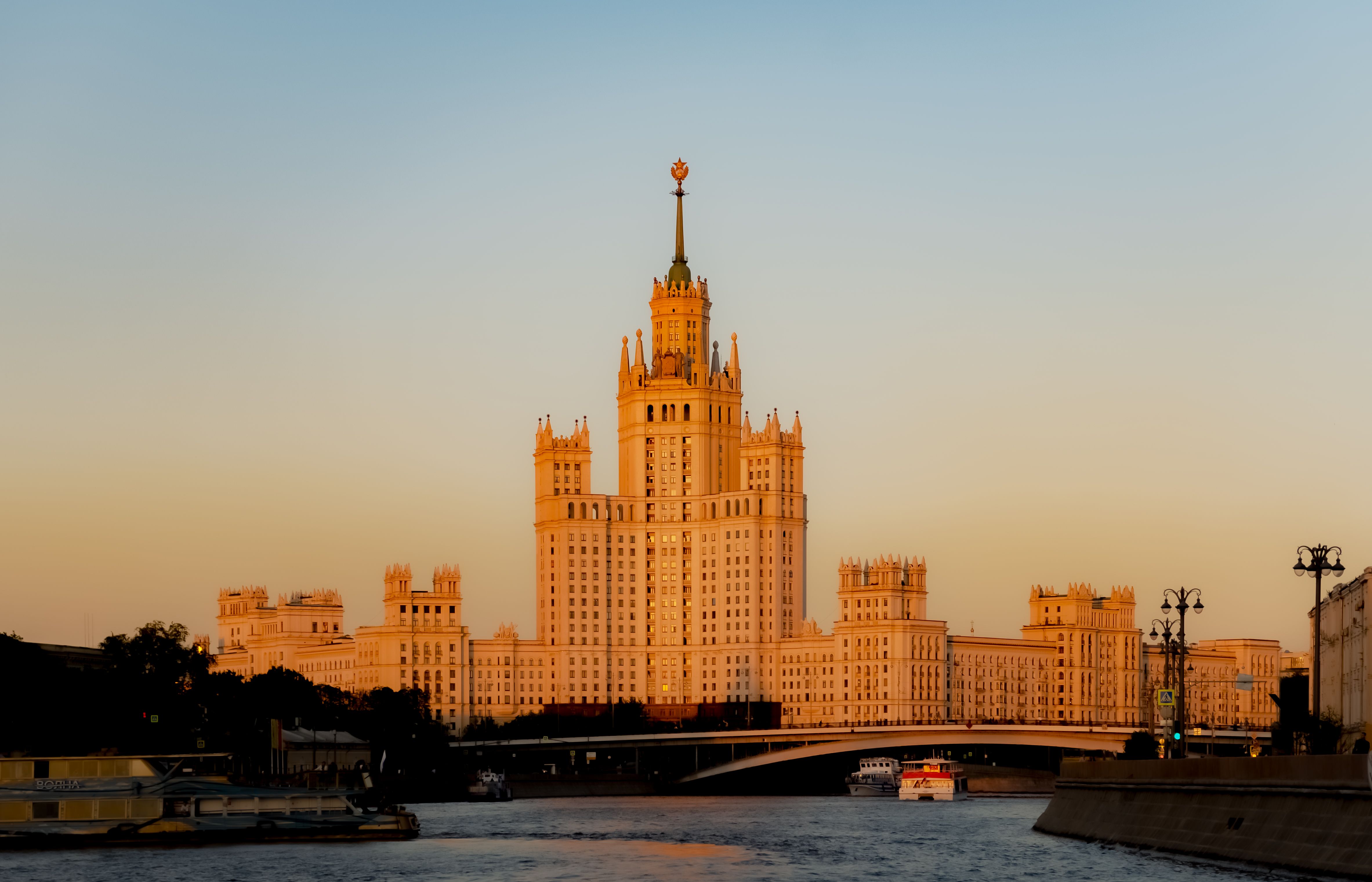A stunning view of a tall, historic building beside the Moskva River, illuminated by warm sunset colors.