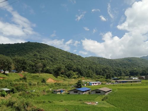 Free A picturesque rural scene featuring lush green hills, scattered houses, and a vibrant blue sky, epitomizing tranquility and nature's beauty. Stock Photo