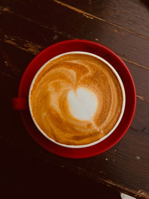 Free A creamy heart-shaped latte art design in a red cup on a rustic table. Stock Photo