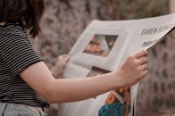 一名女子悠闲地坐在外面，拿着报纸阅读