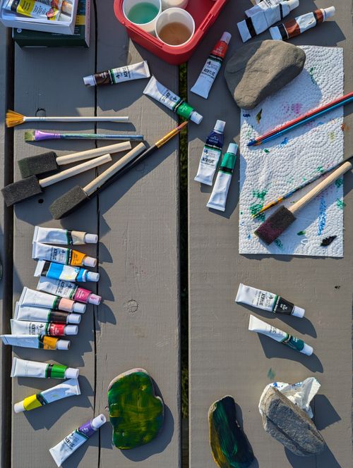 Free A vibrant display of acrylic paints and brushes on a wooden table outdoors. Stock Photo