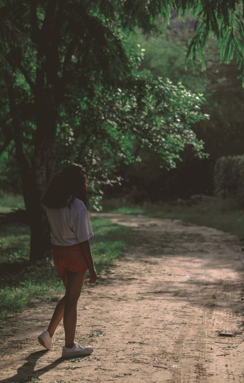 Free A woman strolls through a sunlit forest path, enjoying the serene nature surroundings. Stock Photo