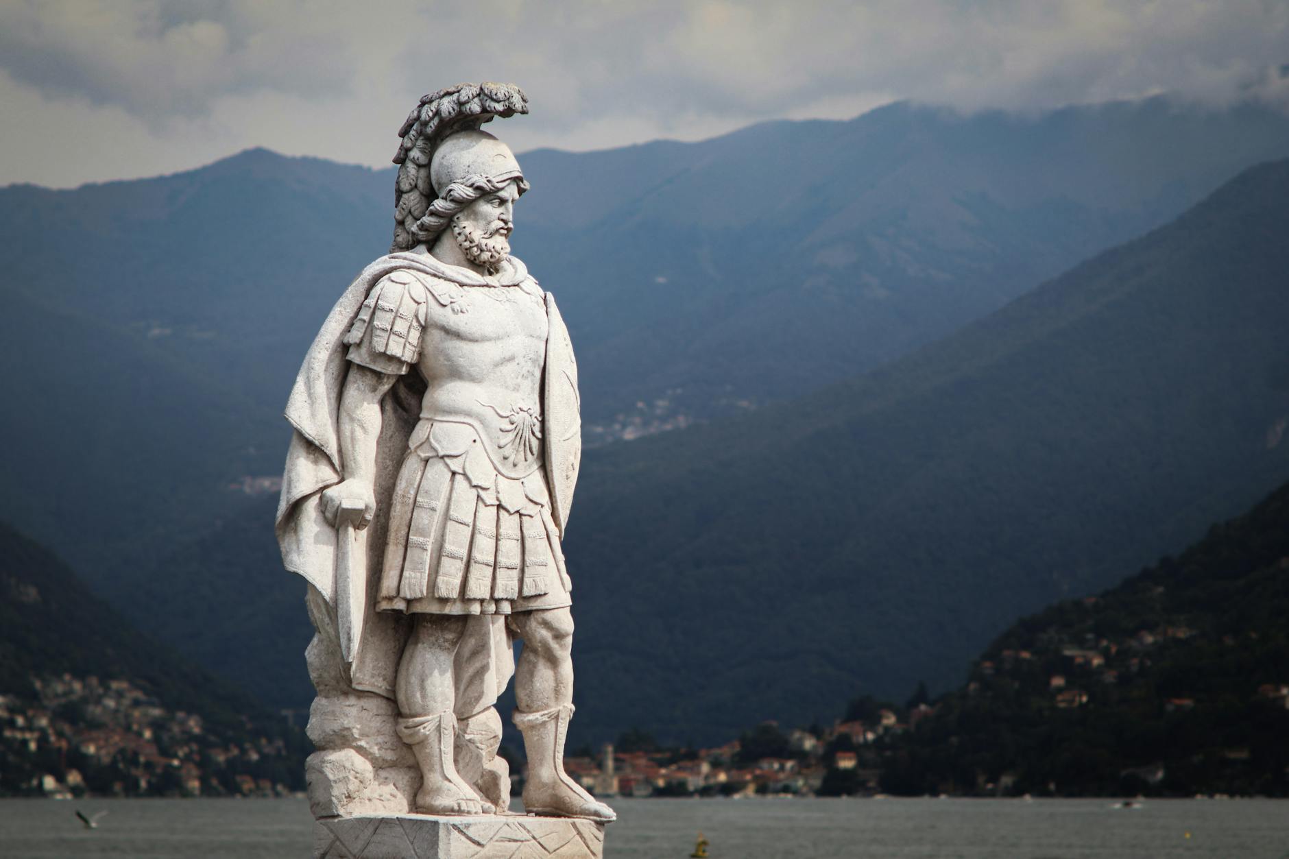 Majestic warrior statue overlooking the serene Lake Como with mountain backdrop.